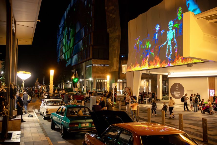 A photo of the precinct at night at Halloween with people and lights on buildings